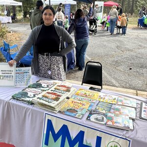 Bright Futures continues to serve over 100 children and caregivers monthly with popular programs like Tiny Tunes and Story. Female standing behind a table with a list of books